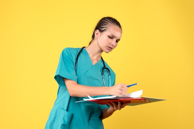 Vista frontale della dottoressa in tuta medica con analisi diverse sulla parete gialla