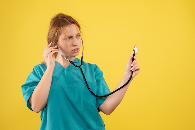 Vista frontale della dottoressa in tuta medica con lo stetoscopio sulla parete gialla