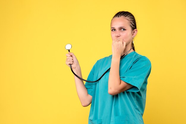 Vista frontale della dottoressa in tuta medica con lo stetoscopio sulla parete gialla