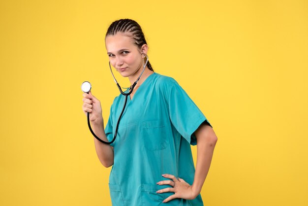 Vista frontale della dottoressa in tuta medica con lo stetoscopio sulla parete gialla