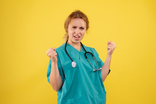 Vista frontale della dottoressa in tuta medica con lo stetoscopio sulla parete gialla