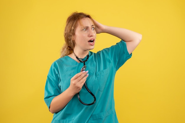 Vista frontale della dottoressa in tuta medica con lo stetoscopio sulla parete gialla