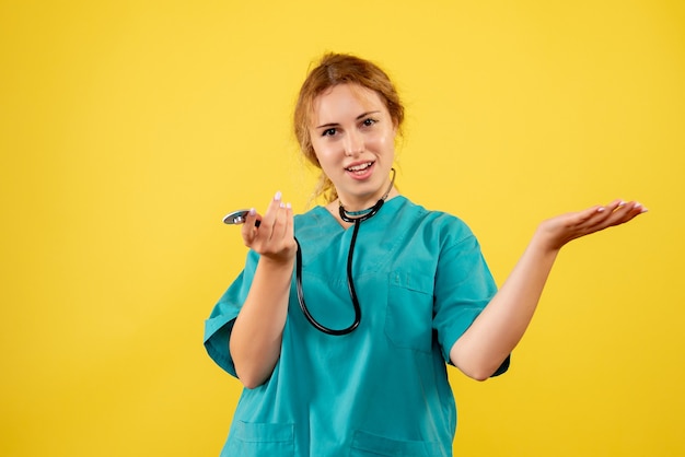 Vista frontale della dottoressa in tuta medica con lo stetoscopio sulla parete gialla