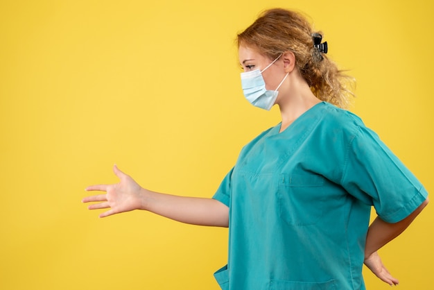Vista frontale della dottoressa in tuta medica e maschera sterile sulla parete gialla