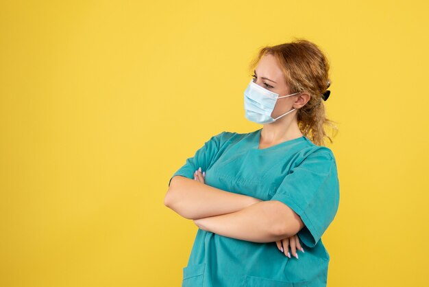 Vista frontale della dottoressa in tuta medica e maschera sulla parete gialla