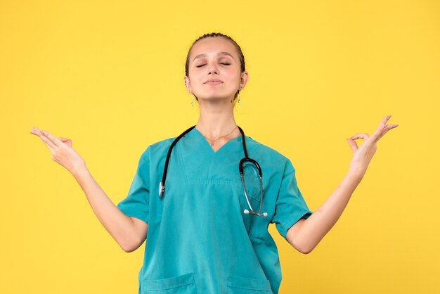 Vista frontale della dottoressa in tuta medica meditando sulla parete gialla