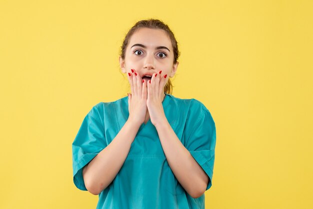 Vista frontale della dottoressa in tuta medica sorpresa sulla parete gialla