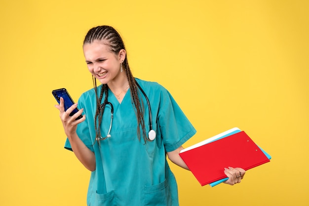 Vista frontale della dottoressa in tuta medica tenendo il telefono sulla parete gialla