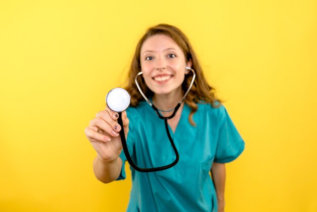 Vista frontale della dottoressa utilizzando uno stetoscopio sulla parete gialla