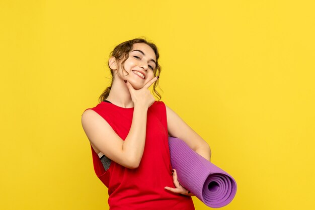 Vista frontale della femmina graziosa che tiene tappeto viola su giallo