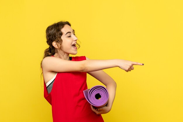 Vista frontale della femmina graziosa che tiene tappeto viola su giallo