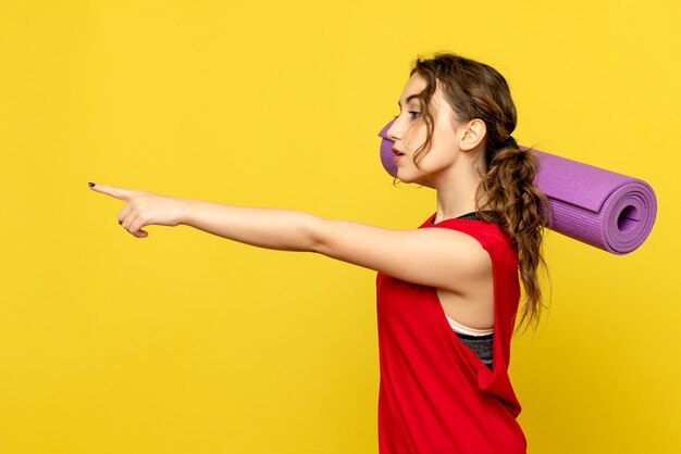 Vista frontale della femmina graziosa che tiene tappeto viola su giallo