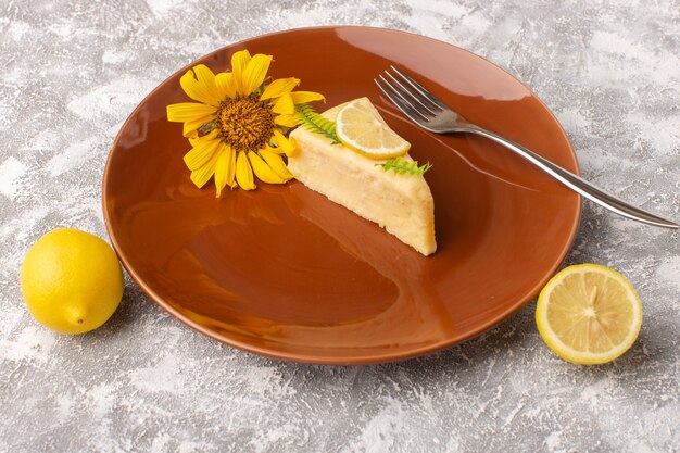 Vista frontale della fetta deliziosa della torta con il limone dentro il piatto marrone sulla superficie della luce