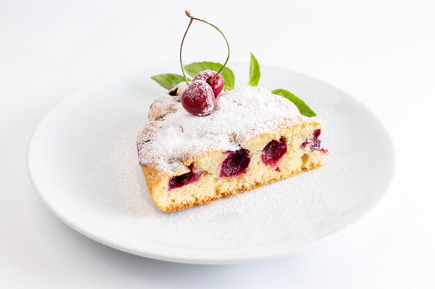 Vista frontale della fetta della torta della ciliegia deliziosa e squisita all'interno del piatto bianco sulla superficie bianca