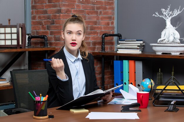 Vista frontale della giovane assistente femminile concentrata seduta alla sua scrivania e in possesso di un documento in ufficio