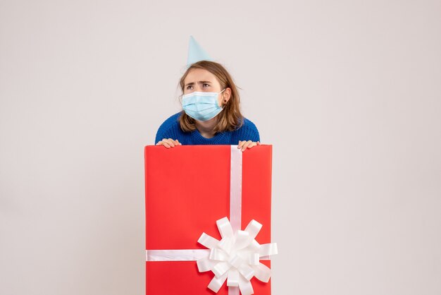 Vista frontale della giovane donna all'interno della confezione regalo in maschera sul muro bianco