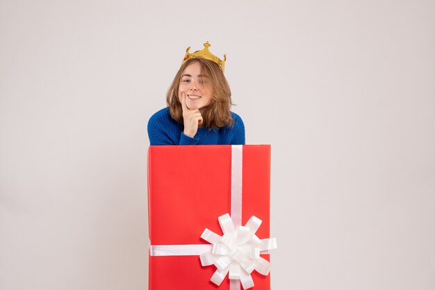 Vista frontale della giovane donna all'interno della scatola regalo rossa sul muro bianco