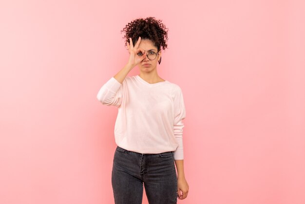 Vista frontale della giovane donna che guarda attraverso le dita sulla parete rosa