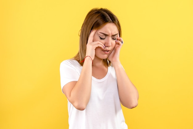 Vista frontale della giovane donna che ha mal di testa sulla parete gialla