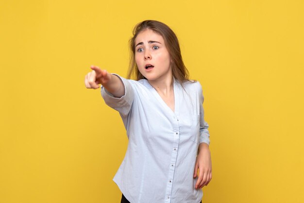 Vista frontale della giovane donna che indica sul muro giallo