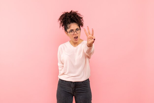 Vista frontale della giovane donna che mostra il numero sulla parete rosa