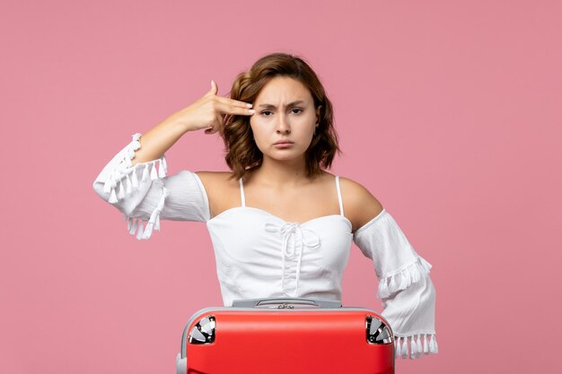 Vista frontale della giovane donna che posa con la borsa rossa delle vacanze sulla parete rosa