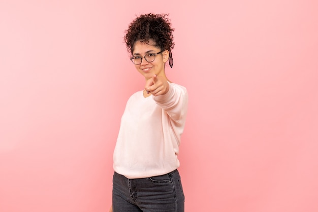 Vista frontale della giovane donna che punta con il sorriso sulla parete rosa