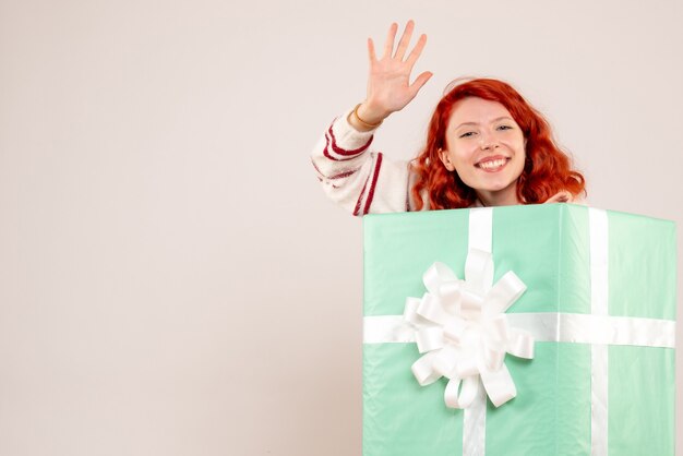 Vista frontale della giovane donna che si nasconde all'interno del regalo di Natale sul muro bianco