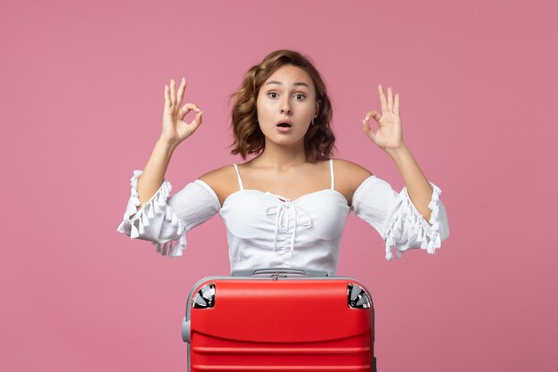 Vista frontale della giovane donna che si prepara per il viaggio con la sua borsa rossa sul muro rosa