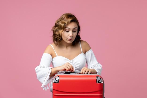 Vista frontale della giovane donna che si prepara per le vacanze con la borsa sulla parete rosa