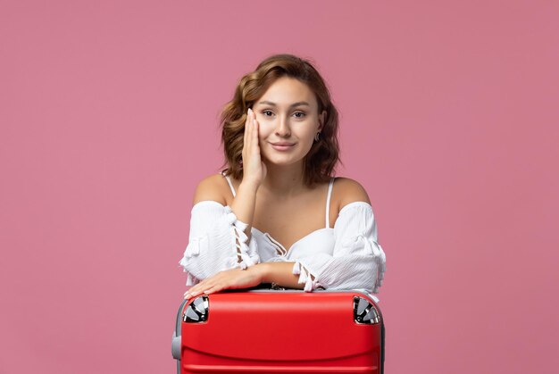 Vista frontale della giovane donna che si prepara per le vacanze con la sua borsa rossa sul muro rosa