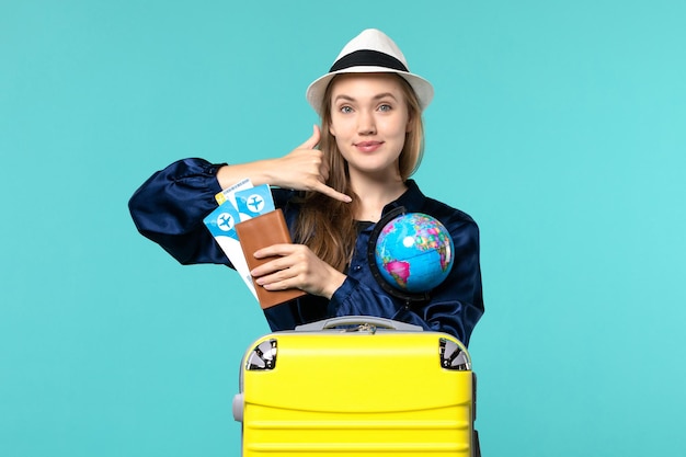Vista frontale della giovane donna che tiene i biglietti e globo che sorridono sul viaggio di viaggio di vacanza del mare del piano del fondo blu