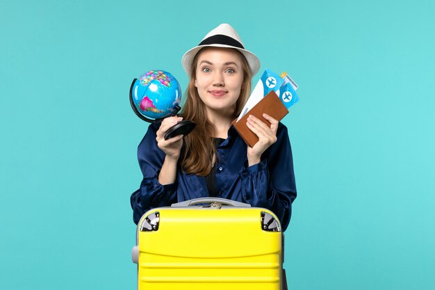 Vista frontale della giovane donna che tiene i biglietti e piccolo globo sul viaggio di viaggio di vacanza del mare dell'aereo del fondo blu