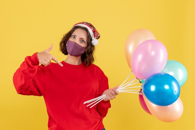 Vista frontale della giovane donna che tiene i palloncini in maschera sulla festa di celebrazione giallo