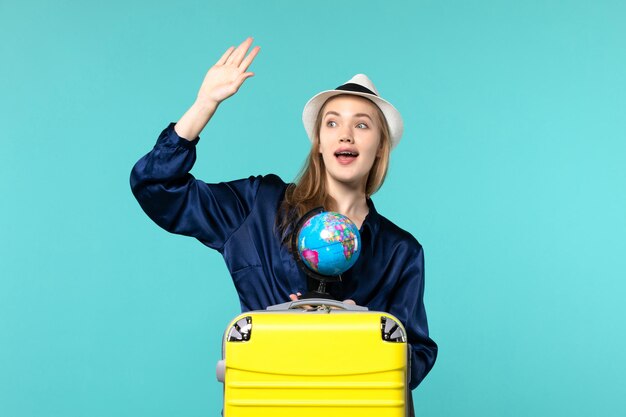 Vista frontale della giovane donna che tiene il globo e si prepara per la vacanza sul mare di viaggio di viaggio di vacanza femminile dell'aereo di sfondo blu