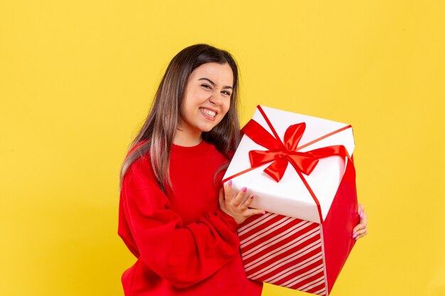Vista frontale della giovane donna che tiene il regalo di Natale nella casella sulla parete gialla