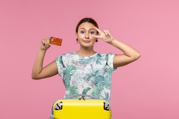 Vista frontale della giovane donna che tiene la carta di credito marrone e posa sul muro rosa
