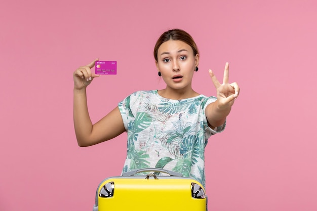 Vista frontale della giovane donna che tiene la carta di credito viola in vacanza sulla scrivania rosa colore viaggio vacanza estate donna