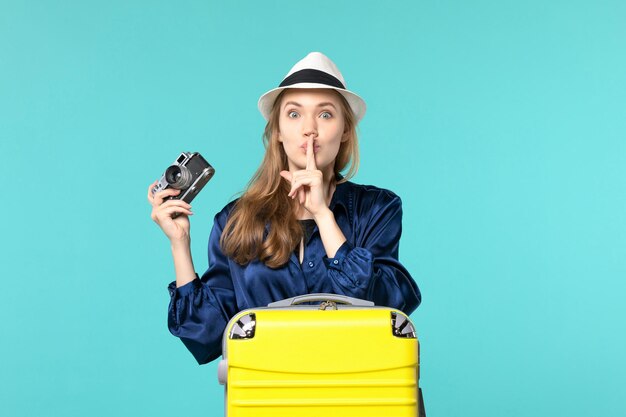 Vista frontale della giovane donna che tiene la macchina fotografica e sorridente sullo sfondo blu donna viaggio viaggio aereo mare