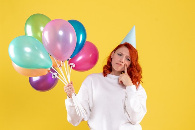 Vista frontale della giovane donna che tiene palloncini colorati carino sulla parete gialla