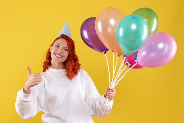 Vista frontale della giovane donna che tiene palloncini colorati carino sulla parete gialla