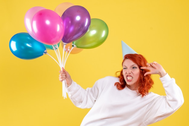 Vista frontale della giovane donna che tiene palloncini colorati carino sulla parete gialla