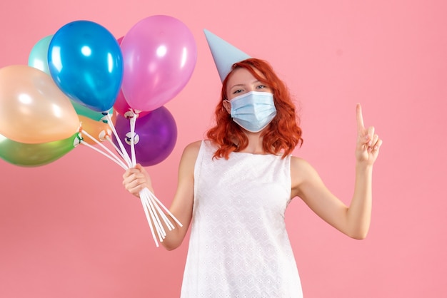 Vista frontale della giovane donna che tiene palloncini colorati in maschera sterile sulla parete rosa