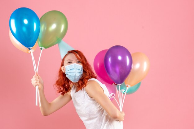 Vista frontale della giovane donna che tiene palloncini colorati in maschera sterile sulla parete rosa