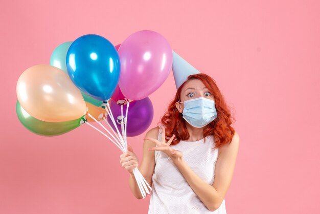 Vista frontale della giovane donna che tiene palloncini colorati in maschera sterile sulla parete rosa