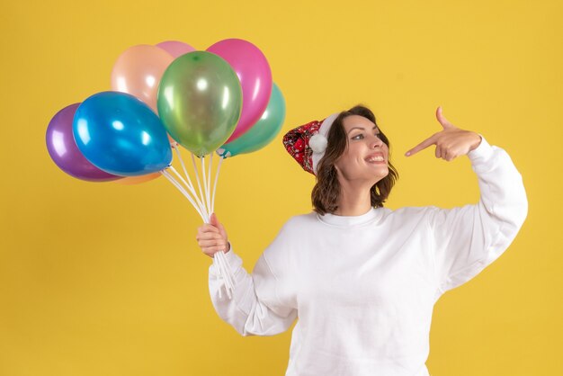 Vista frontale della giovane donna che tiene palloncini colorati sulla parete gialla