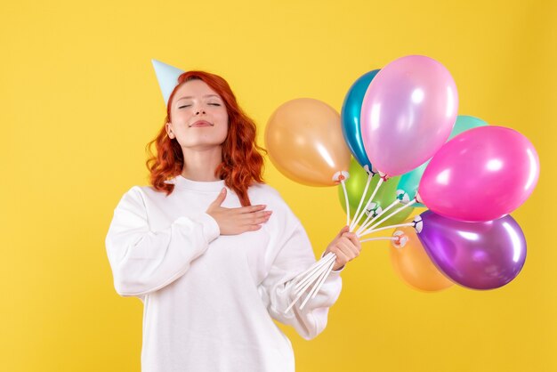 Vista frontale della giovane donna che tiene palloncini colorati sulla parete gialla