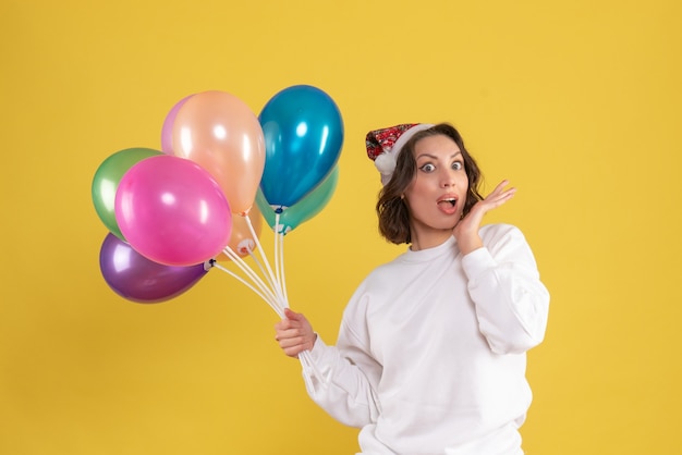 Vista frontale della giovane donna che tiene palloncini colorati sulla parete gialla