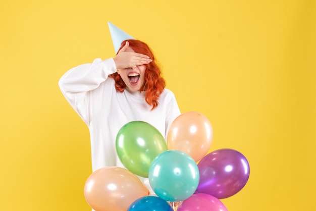 Vista frontale della giovane donna che tiene palloncini colorati sulla parete gialla