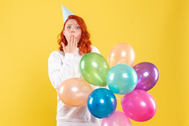 Vista frontale della giovane donna che tiene palloncini colorati sulla parete gialla